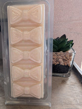 Load image into Gallery viewer, Packaged bow-shaped wax melts on a wooden surface with a plant in the background